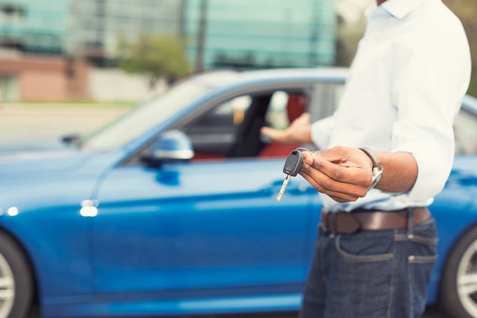 person holding car keys offering used blue car on background