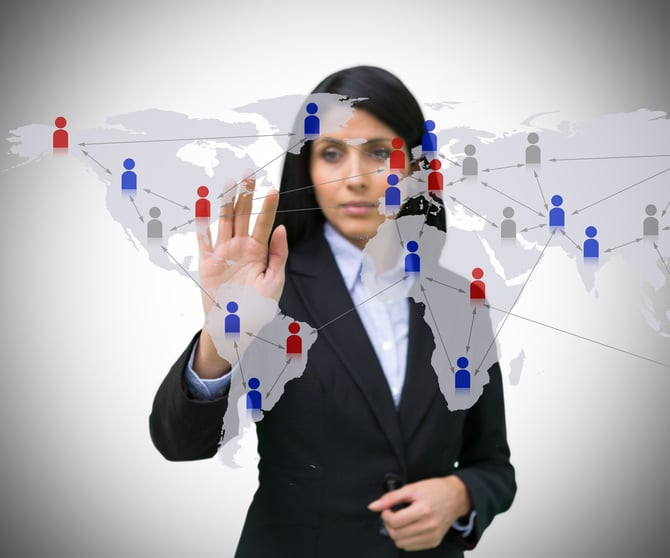 A businesswoman in a suit touches a world map interface with red and blue people icons on it.
