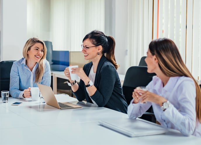 Smiling business people at a desk with laptops and coffee 